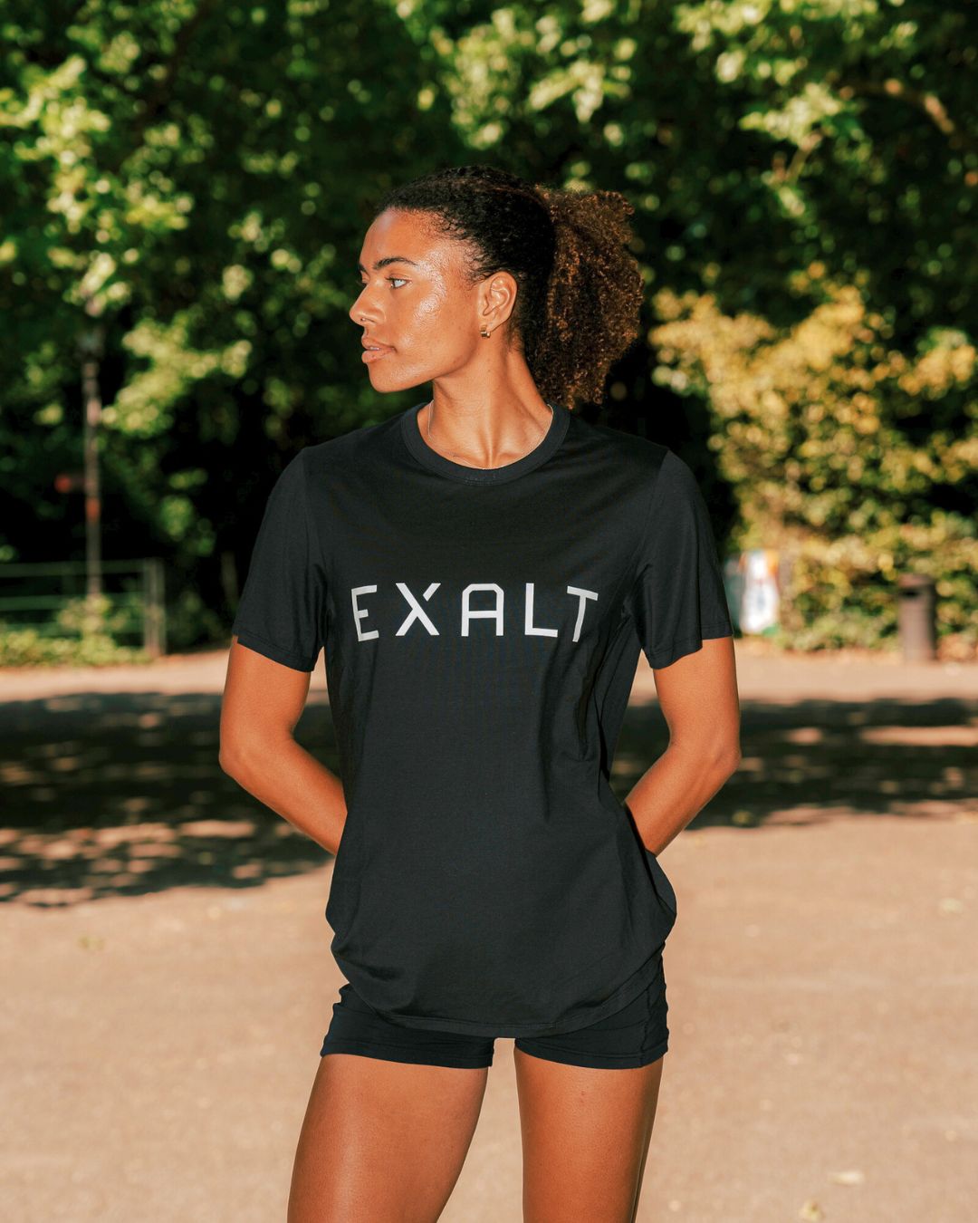 Angle shot of Women wearing Black EXALT x Lululemon Fundamental Tee in a park with trees in the background.