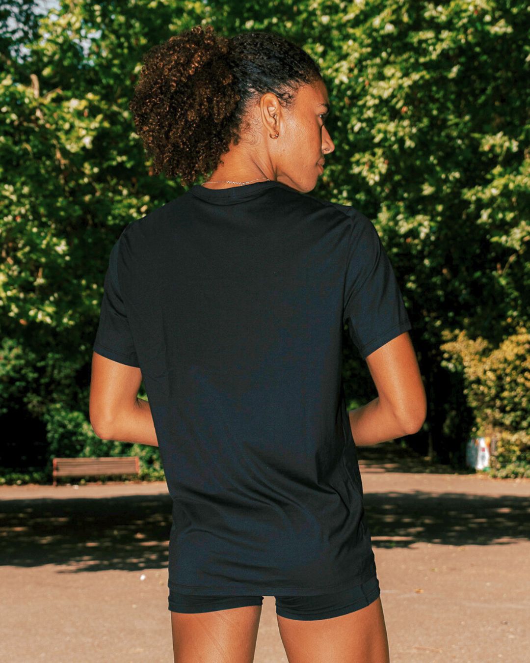 Back shot of Women wearing Black EXALT x Lululemon Fundamental Tee in a park with trees in the background.