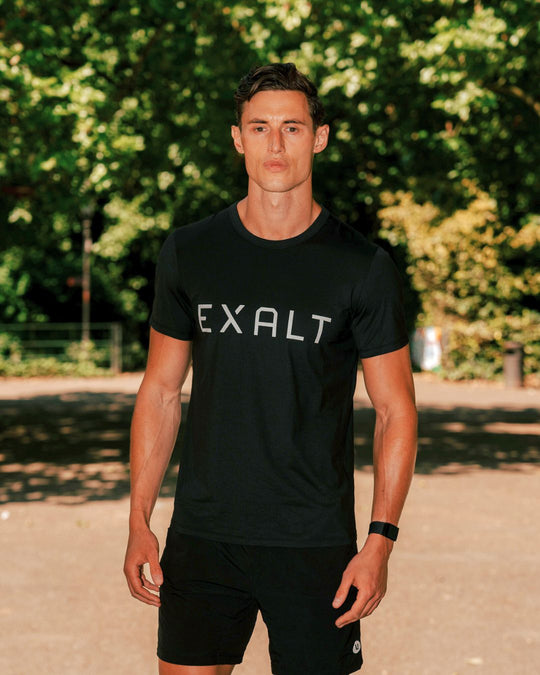 Front shot of Man wearing Black EXALT x Lululemon Fundamental Tee in a park with trees in the background.